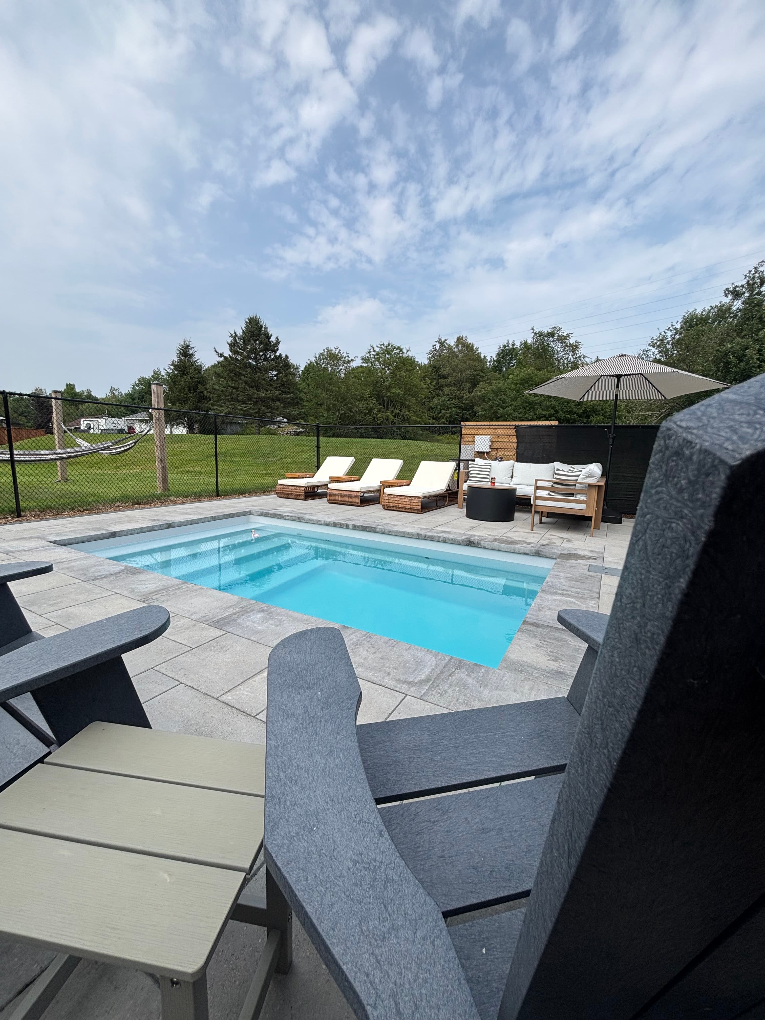 Fiberglass pool with paver deck and forest backdrop