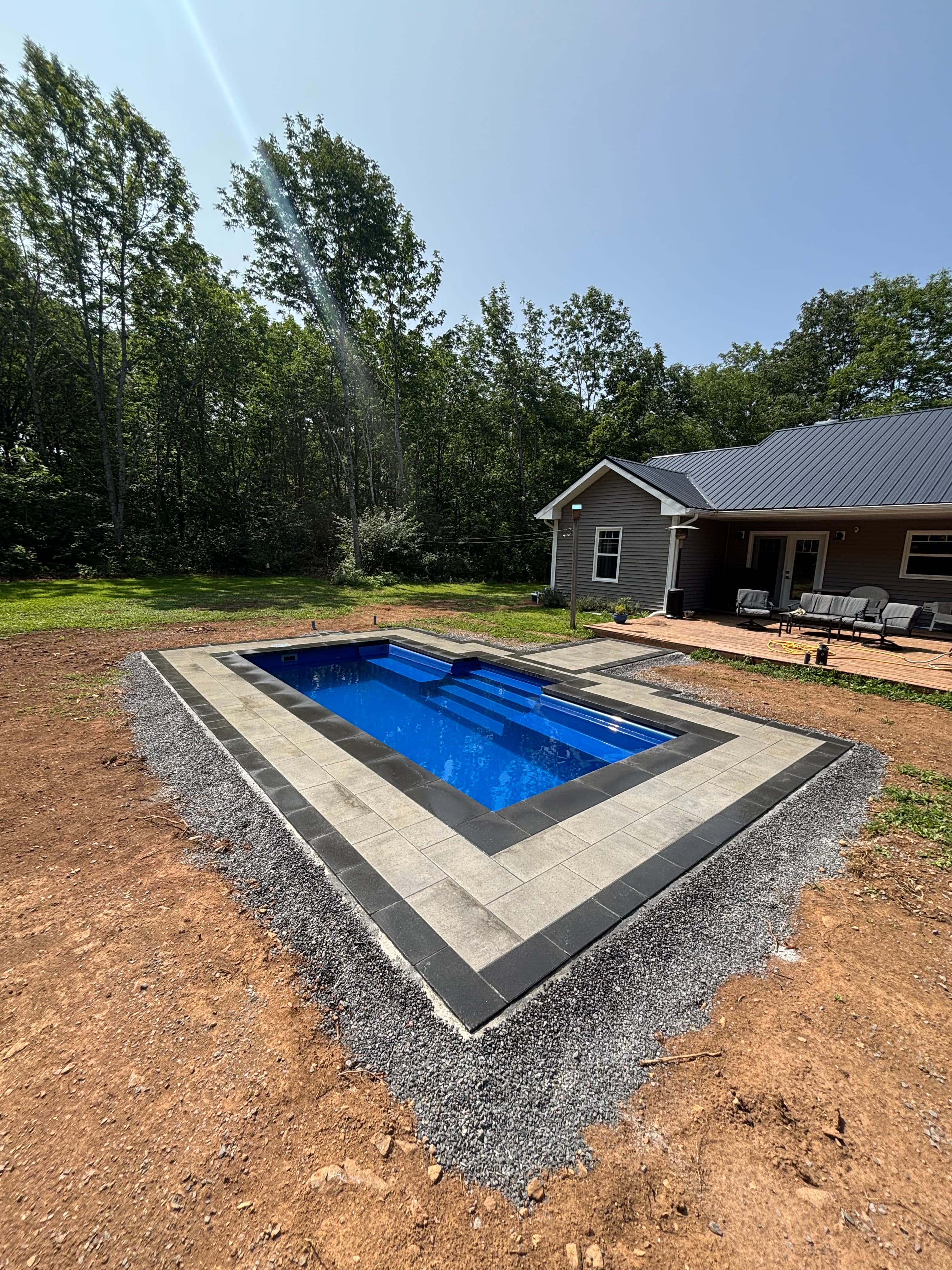 Large blue fiberglass pool behind grey country home